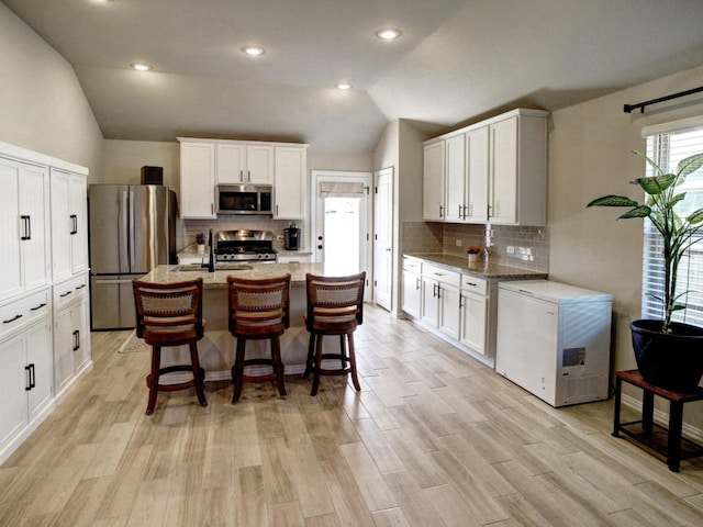116 Shagbark Trl, Bastrop, TX 78602 - kitchen featuring stainless steel appliances, vaulted ceiling, decorative backsplash, white cabinets, and light stone countertops