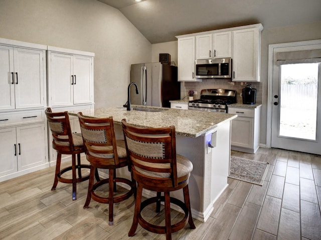 kitchen featuring lofted ceiling, white cabinetry, stainless steel appliances, an island with sink, and sink