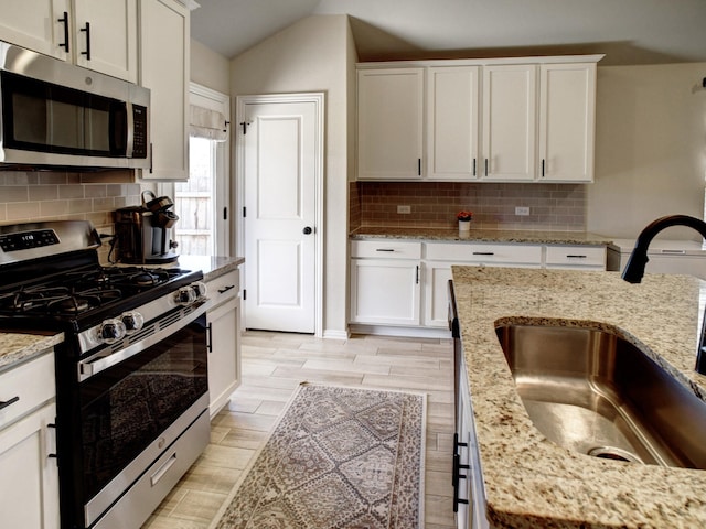 kitchen with stainless steel appliances, white cabinetry, light stone counters, and sink