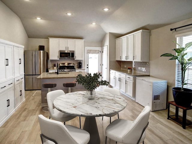 116 Shagbark Dr, Bastrop, TX 78602 - kitchen featuring stainless steel appliances, vaulted ceiling, decorative backsplash, a kitchen island with sink, and white cabinetry