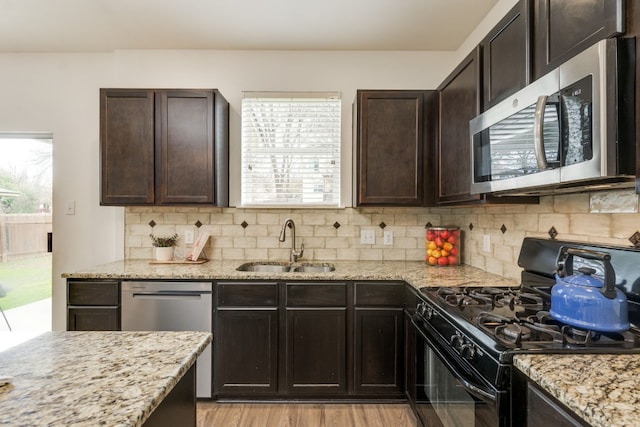 kitchen with dark brown cabinetry, sink, tasteful backsplash, light stone counters, and appliances with stainless steel finishes