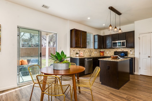 kitchen with a kitchen island, appliances with stainless steel finishes, pendant lighting, dark brown cabinetry, and light wood-type flooring