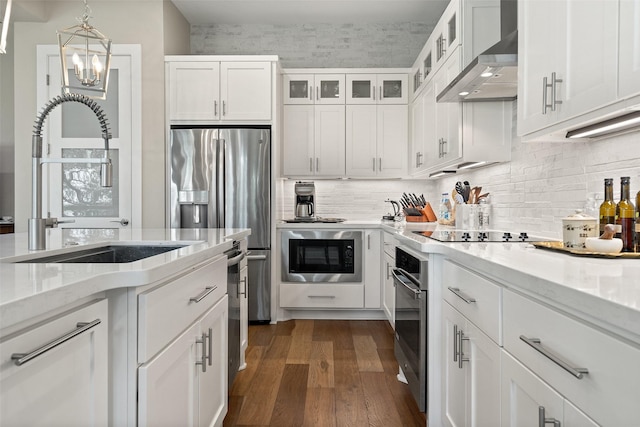 kitchen featuring black appliances, wall chimney exhaust hood, white cabinets, light stone counters, and sink