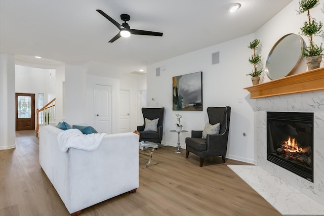 living room with ceiling fan, a high end fireplace, and light hardwood / wood-style flooring