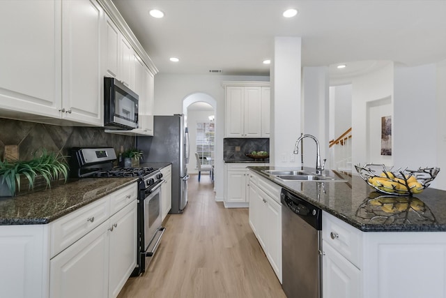 kitchen with white cabinets, stainless steel appliances, dark stone counters, sink, and light wood-type flooring