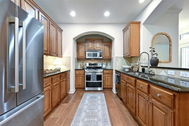 kitchen featuring tasteful backsplash, sink, light wood-type flooring, stainless steel appliances, and dark stone counters