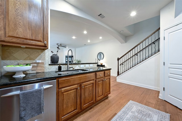 kitchen featuring decorative backsplash, dishwasher, dark stone counters, light hardwood / wood-style flooring, and sink