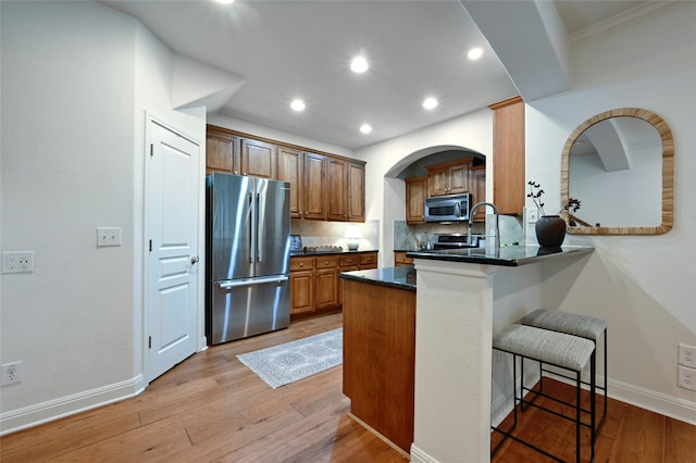 kitchen with a kitchen bar, kitchen peninsula, appliances with stainless steel finishes, backsplash, and light hardwood / wood-style flooring