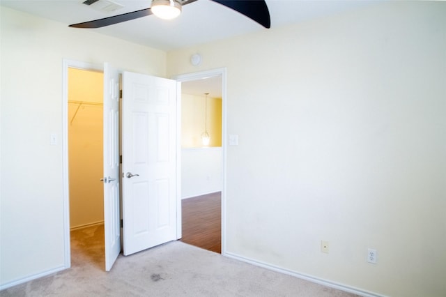 unfurnished bedroom featuring a walk in closet, ceiling fan, light carpet, and a closet