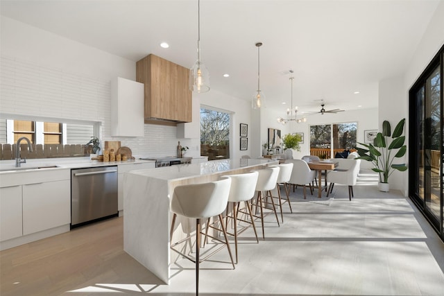 kitchen featuring white cabinetry, ceiling fan, a kitchen island, stainless steel dishwasher, and sink