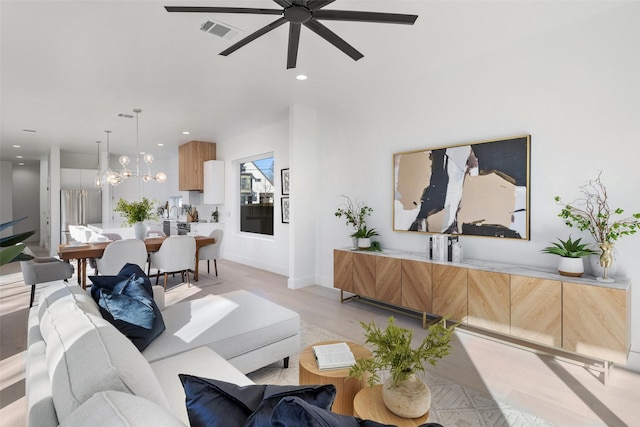 living room featuring ceiling fan with notable chandelier and light hardwood / wood-style flooring