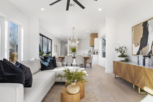 living room with ceiling fan with notable chandelier and light hardwood / wood-style floors