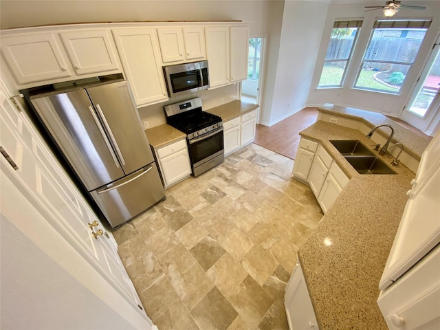 kitchen featuring ceiling fan, appliances with stainless steel finishes, white cabinets, light stone counters, and sink