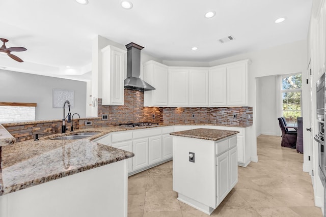 kitchen featuring sink, white cabinets, a center island, light stone counters, and wall chimney range hood