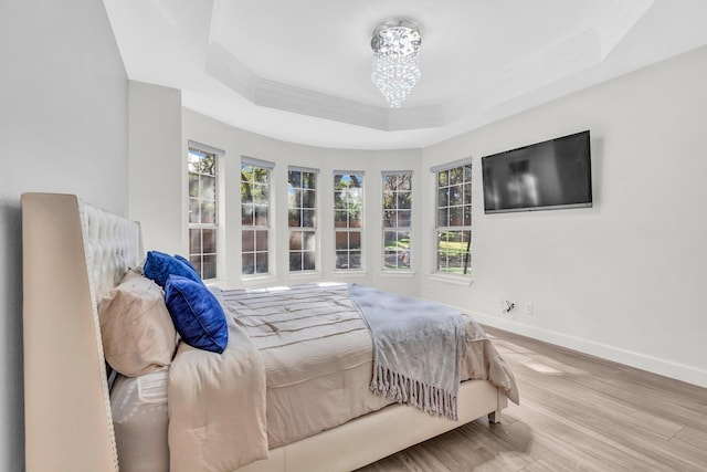 bedroom with a notable chandelier, a tray ceiling, and light wood-type flooring