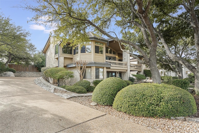 view of front of house featuring stone siding, a balcony, and fence