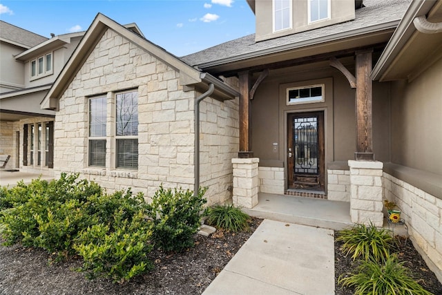 doorway to property featuring stone siding and a shingled roof