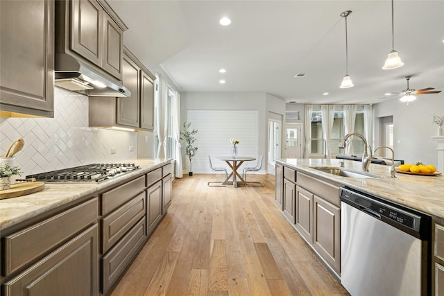 kitchen featuring stainless steel appliances, decorative backsplash, light hardwood / wood-style flooring, light stone counters, and sink