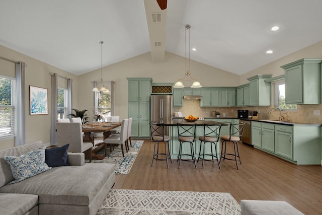 kitchen with sink, hanging light fixtures, green cabinetry, stainless steel appliances, and light hardwood / wood-style flooring