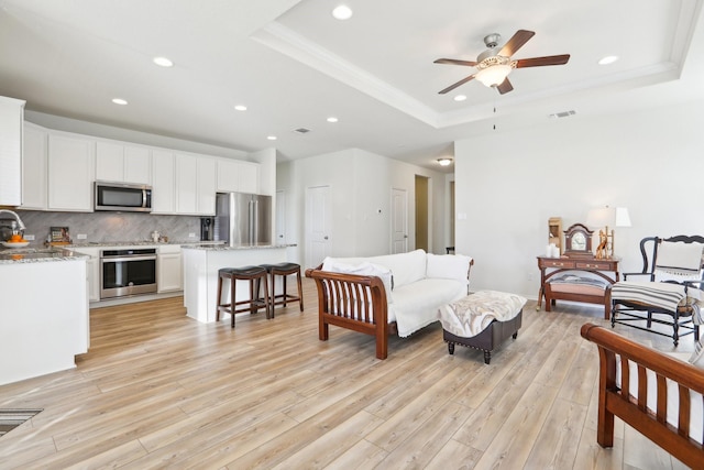 living room featuring ceiling fan, a tray ceiling, light wood-type flooring, crown molding, and sink