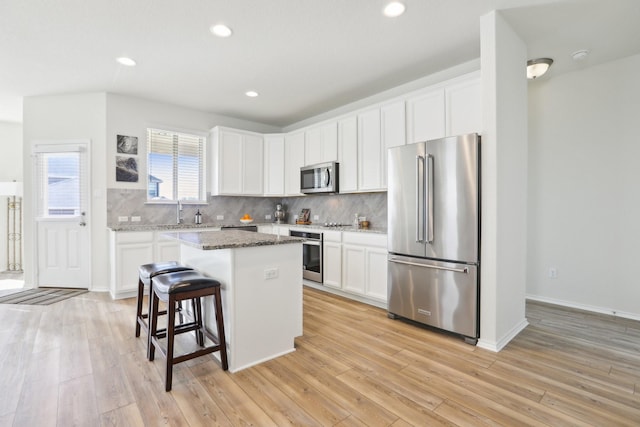 kitchen with white cabinets, a center island, a kitchen bar, stainless steel appliances, and stone countertops