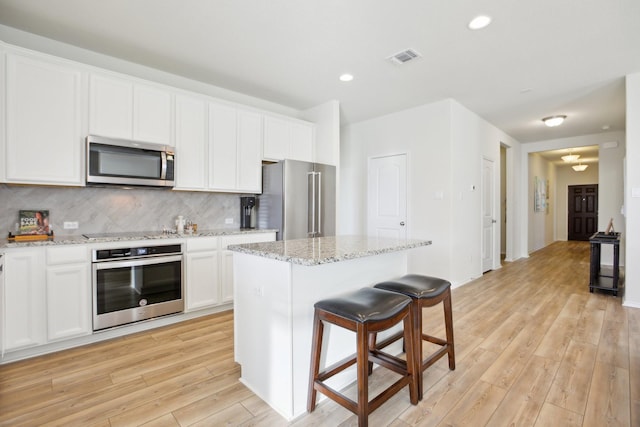 kitchen featuring a kitchen island, decorative backsplash, white cabinetry, appliances with stainless steel finishes, and light stone counters