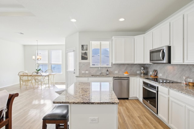 kitchen featuring a center island, sink, hanging light fixtures, stainless steel appliances, and white cabinets