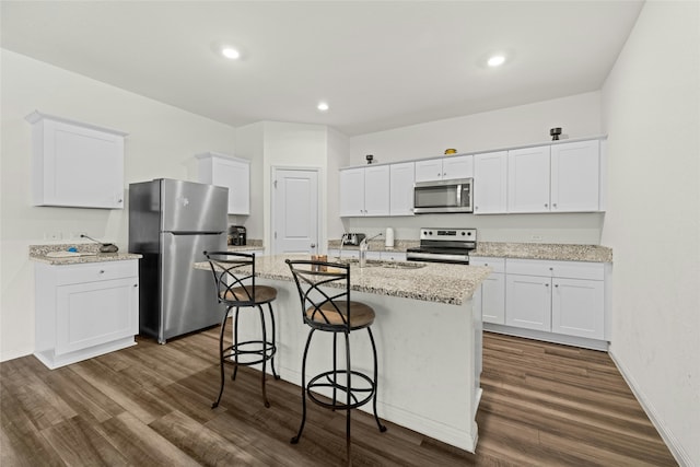 kitchen featuring white cabinetry, an island with sink, stainless steel appliances, dark wood-type flooring, and light stone counters