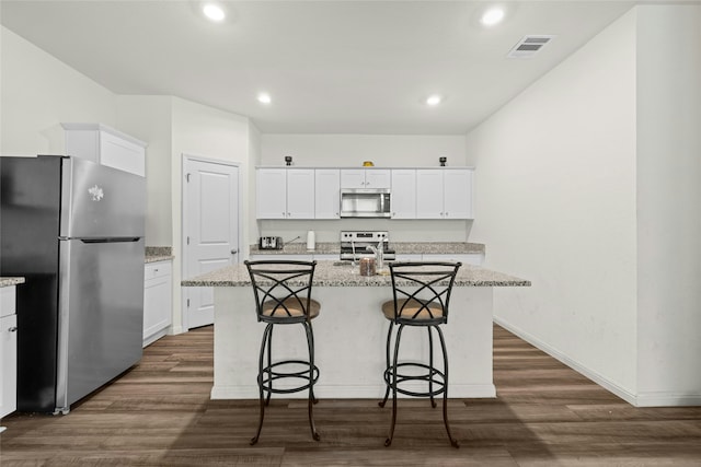 kitchen featuring white cabinets, a kitchen island with sink, appliances with stainless steel finishes, and light stone counters