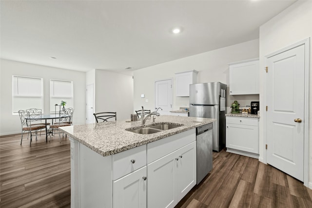 kitchen with an island with sink, stainless steel appliances, white cabinets, light stone counters, and sink