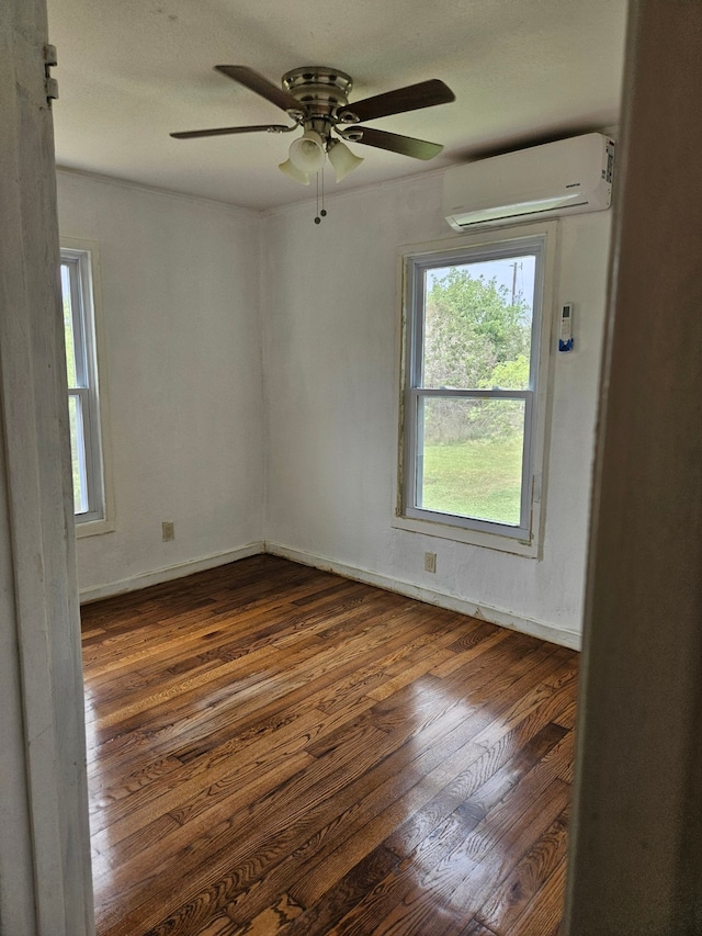 unfurnished room featuring ceiling fan, an AC wall unit, dark wood-type flooring, and plenty of natural light