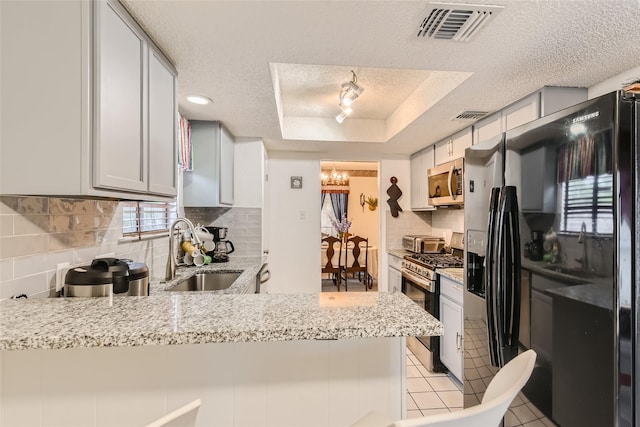 kitchen with a raised ceiling, kitchen peninsula, appliances with stainless steel finishes, a textured ceiling, and a chandelier