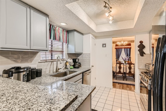 kitchen with a raised ceiling, decorative backsplash, sink, an inviting chandelier, and stainless steel appliances