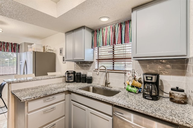 kitchen featuring backsplash, stainless steel dishwasher, fridge, sink, and a textured ceiling