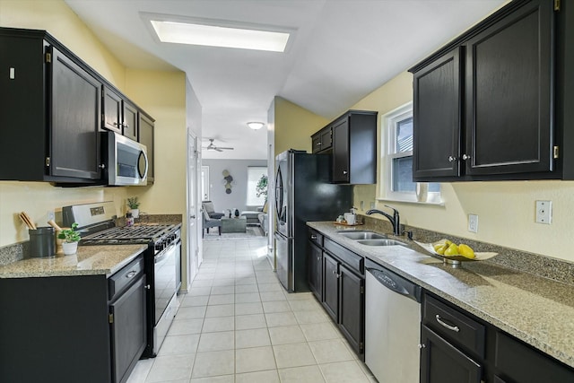 kitchen with light tile patterned floors, ceiling fan, appliances with stainless steel finishes, light stone counters, and sink