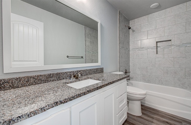 full bathroom featuring a textured ceiling, tiled shower / bath, vanity, toilet, and hardwood / wood-style flooring