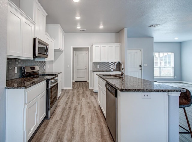 108 Elmer Ave, Burnet, TX 78611 - kitchen featuring appliances with stainless steel finishes, light wood-type flooring, backsplash, a breakfast bar, and white cabinetry