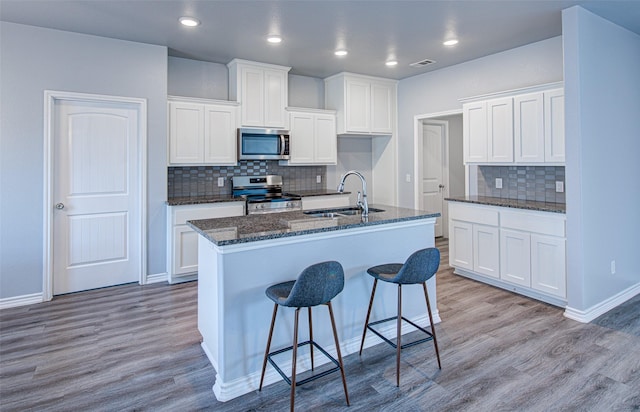 kitchen with stainless steel appliances, sink, white cabinets, and a kitchen island with sink