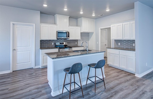 108 Elmer Ave, Burnet, TX 78611 - kitchen with appliances with stainless steel finishes, wood finished floors, decorative backsplash, a kitchen island with sink, and recessed lighting