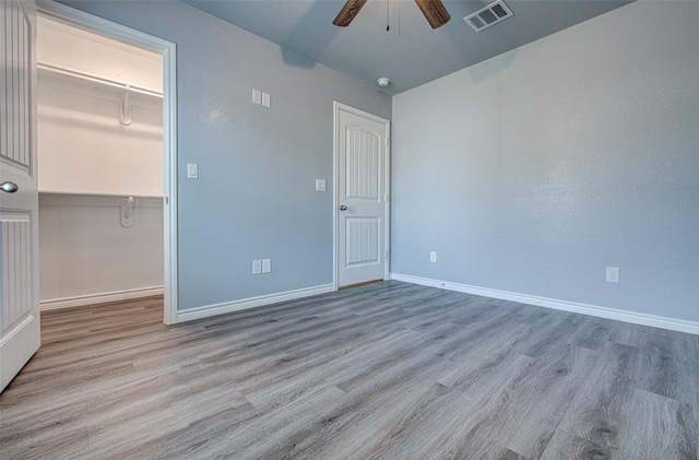 unfurnished bedroom with ceiling fan, a walk in closet, a closet, and light wood-type flooring