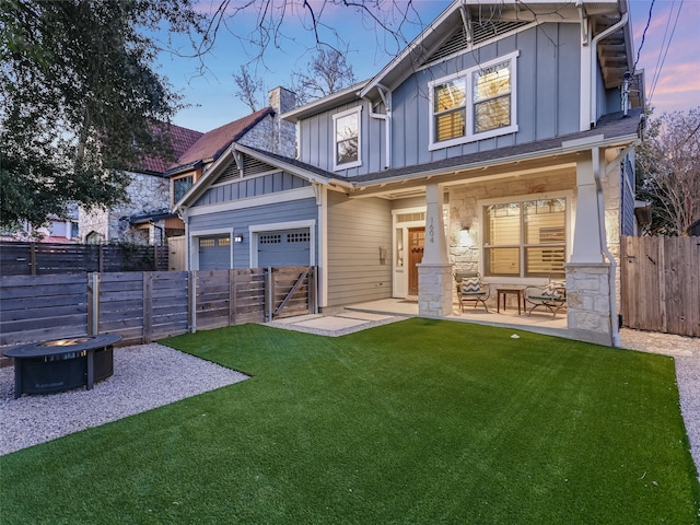 back house at dusk with a garage, an outdoor fire pit, and a yard