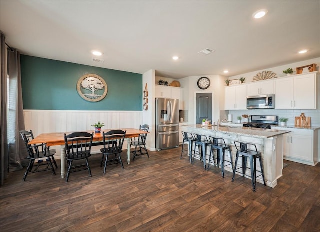 kitchen with dark wood-type flooring, light stone counters, a center island with sink, stainless steel appliances, and white cabinets