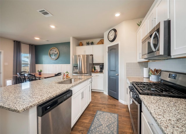 kitchen with sink, dark wood-type flooring, appliances with stainless steel finishes, white cabinetry, and a center island with sink