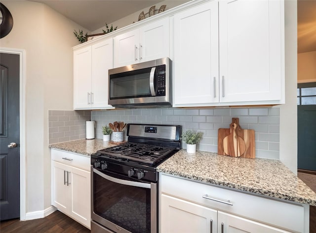 kitchen with appliances with stainless steel finishes, light stone counters, white cabinets, dark hardwood / wood-style flooring, and decorative backsplash