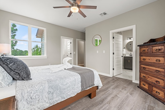 bedroom with a ceiling fan, baseboards, visible vents, ensuite bath, and light wood-style flooring