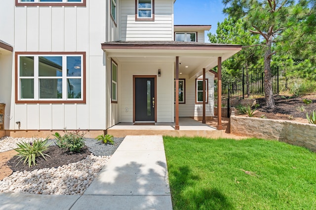 view of exterior entry featuring a lawn, board and batten siding, and fence