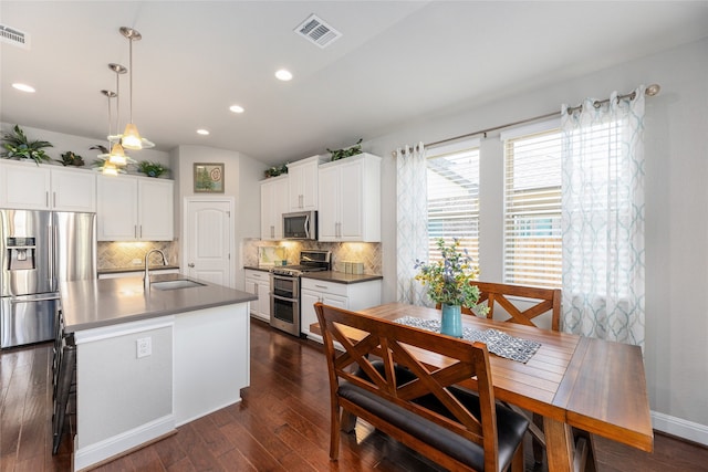 kitchen with decorative light fixtures, white cabinetry, stainless steel appliances, an island with sink, and sink