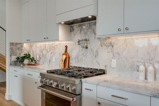 kitchen featuring high end stainless steel range oven, premium range hood, light hardwood / wood-style floors, backsplash, and light stone counters