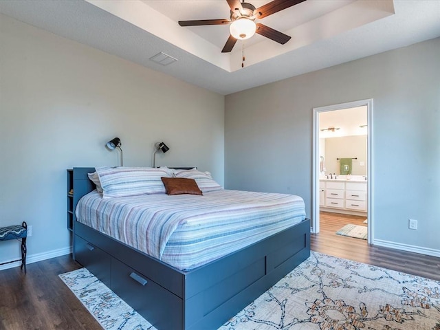 bedroom featuring dark wood-type flooring, ceiling fan, ensuite bathroom, and a tray ceiling