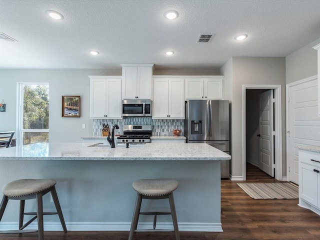 kitchen featuring a center island with sink, stainless steel appliances, backsplash, dark wood-type flooring, and white cabinets